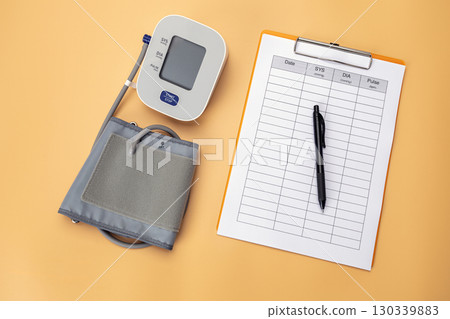 Blood pressure monitor with a data recording pad and pen is placed on the table, showing that it is a practice of self care by recording daily health data. 130339883