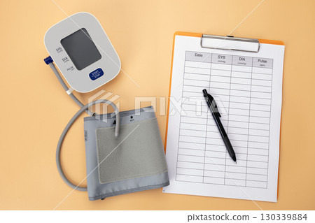 Blood pressure monitor with a data recording pad and pen is placed on the table, showing that it is a practice of self care by recording daily health data. Blood pressure monitor with a data recording pad and pen is placed on the table, showing that it is a practice of self care by recording daily health data. 130339884