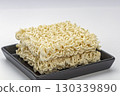 Uncooked instant noodle block on black plate raw ramen square dry wavy pasta beige color simple food minimal style studio light clean background comfort mood close up 130339890