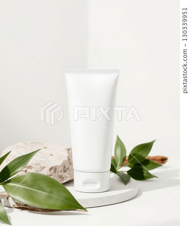 A white cosmetic tube with a minimalistic design on a stone and leaves. 130339951