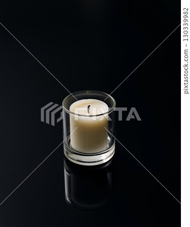 A beautifully lit candle in a clear glass holder, reflecting on a glossy black surface. A beautifully lit candle in a clear glass holder, reflecting on a glossy black surface. 130339982