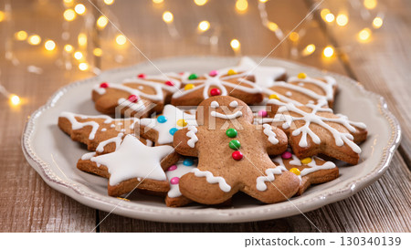 Christmas gingerbread cookies with icing and colorful candy decorations arranged on a plate with festive lights in the background 130340139