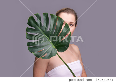 Caucasian adult female partially hidden behind large monstera leaf on gray Caucasian adult female partially hidden behind large monstera leaf on gray 130340674