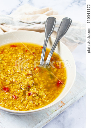 Delicious bowl of golden lentil soup with spices and red pepper flakes presented on a rustic wooden surface 130341172
