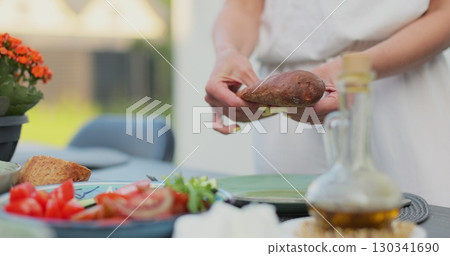 Woman eating at table in a Backyard. Outdoor lunch, barbecue. Garden party celebration in a backyard. Young people have fun, eat and drink sunny summer day. 130341690