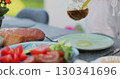Woman eating at table in a Backyard. Outdoor lunch, barbecue. Garden party celebration in a backyard. Young people have fun, eat and drink sunny summer day. 130341696