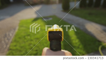 Man spraying green grass lawn with sprayer. Gardening, waters, growing and plants care. 130341713