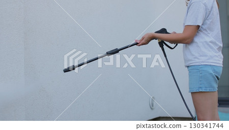 Young woman wash house wall with pressure washer. 130341744
