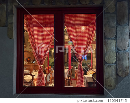 Red window with checkered curtain showing warm interior of a rustic cafe. Tradition, culture, and hospitality reflected through dining atmosphere and vintage interior design. Red window with checkered curtain showing warm interior of a rustic cafe. Tradition, culture, and hospitality reflected through dining atmosphere and vintage interior design. 130341745