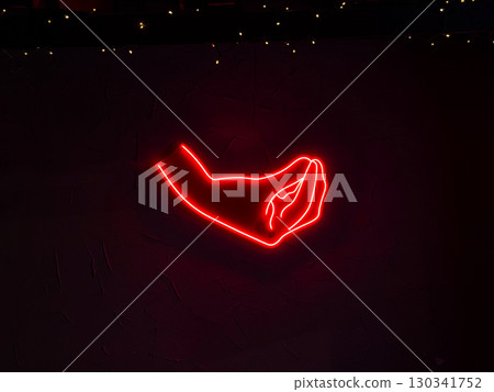Red neon sign in shape of a hand glowing on dark wall with small lights. Nightlife, art, and culture expressed through design, illumination, and urban entertainment. Red neon sign in shape of a hand glowing on dark wall with small lights. Nightlife, art, and culture expressed through design, illumination, and urban entertainment. 130341752