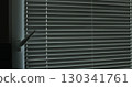 Woman closes the blinds. Metal blinds that close on large windows in the interior. 130341761