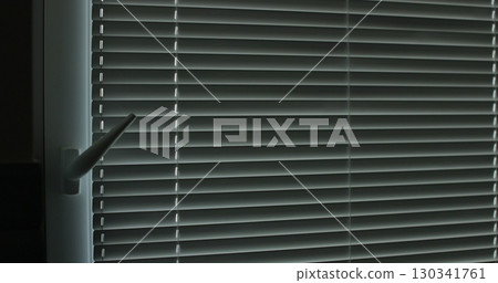 Woman closes the blinds. Metal blinds that close on large windows in the interior. 130341761