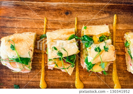 Sandwich portions with fresh vegetables on wooden tray. Culinary presentation, nutrition, and gourmet lifestyle in cafe dining experience. Sandwich portions with fresh vegetables on wooden tray. Culinary presentation, nutrition, and gourmet lifestyle in cafe dining experience. 130341952