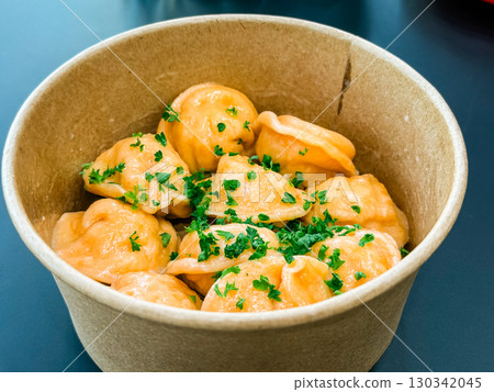 Portion of dumplings served in eco-friendly paper bowl with parsley garnish on top. Traditional cuisine, meal and food preparation representing dining, catering and takeaway service. 130342045