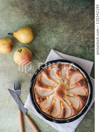 Pear pie in dark mold, fresh pears, knife and fork on textured background. Composition and subdued lighting create cozy and rustic atmosphere perfect for food blogs, recipe sites or culinary magazines Pear pie in dark mold, fresh pears, knife and fork on textured background. Composition and subdued lighting create cozy and rustic atmosphere perfect for food blogs, recipe sites or culinary magazines 130342195