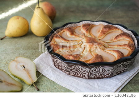 Delicious homemade cottage cheese and pear pie in ceramic baking dish on textured green surface. Warm cozy atmosphere is perfect for food and lifestyle content Delicious homemade cottage cheese and pear pie in ceramic baking dish on textured green surface. Warm cozy atmosphere is perfect for food and lifestyle content 130342196