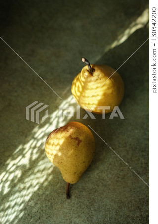 Two fresh pears on textured green-grey background with sunlight casting shadows on fruit, highlighting its organic texture and shape. Perfect for food, lifestyle or fall-themed content 130342200