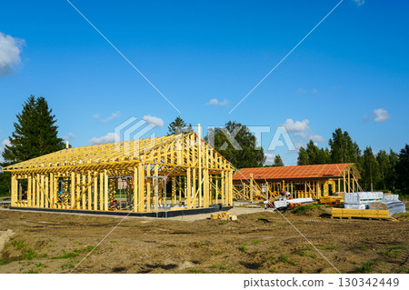 Wooden frame houses under construction with roof trusses and building materials on construction site 130342449