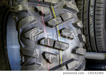 Close-up of rugged ATV tire tread pattern with colored markings, displayed among other vehicle tires 130342460