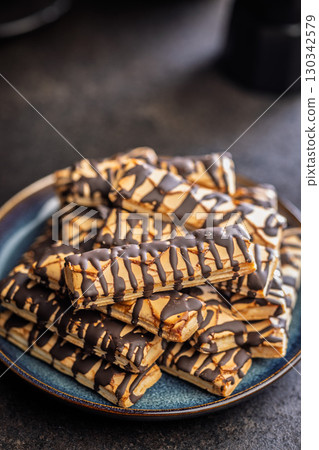 Sfogliatine glassate with chocolate. Italian crispy dessert on plate on black table. 130342579