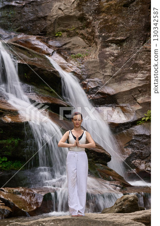 woman performing slow tai chi movements near a waterfall and river at sunset capturing harmony balance and fitness in nature 130342587