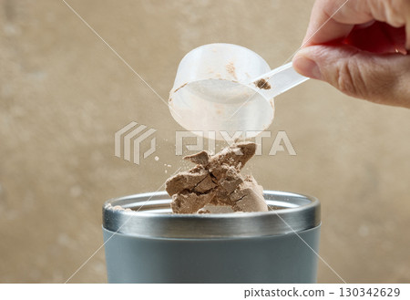 protein powder spills in cup from measure scoop.  whey sports nutrition. dry mixture 130342629