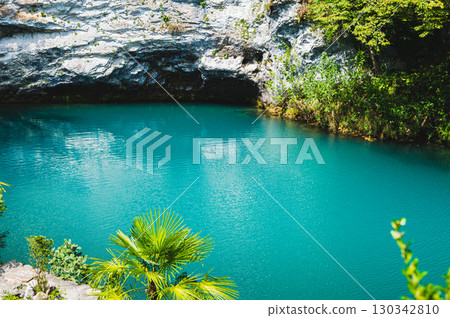 Grotto and blue clear mountain lake with vegetation along the banks 130342810