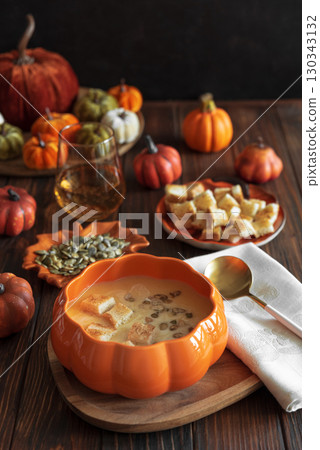 Creamy pumpkin soup with croutons and seeds, served in a pumpkin-shaped bowl on dark wooden table. 130343132