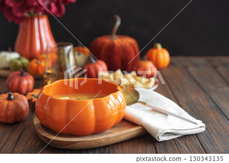 Creamy pumpkin soup with croutons and seeds, served in a pumpkin-shaped bowl on dark wooden table. Creamy pumpkin soup with croutons and seeds, served in a pumpkin-shaped bowl on dark wooden table. 130343135