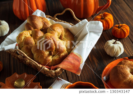 Autumnal tea set with baked buns into basket, pumpkin-shaped teapot and mug on a wooden table. 130343147