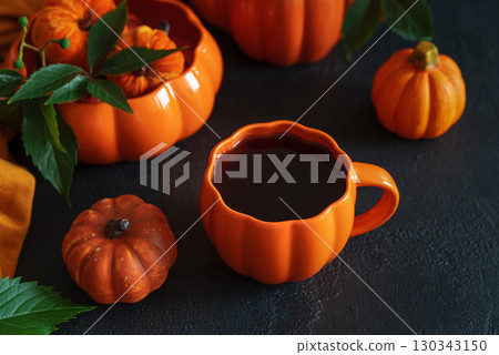 Autumnal tea set with pumpkin-shaped teapot and mug, and decorative pumpkins on a black wooden table. 130343150