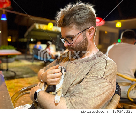 Man looking at kitten with mutual gaze in close moment. Intimacy, trust, and human animal connection with companionship, affection, and emotional bond 130343323