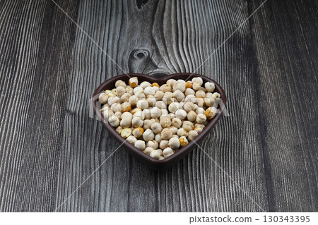 Roasted white chickpeas in wooden bowl on wooden background, top view. White chickpeas, with their high fiber content, are very healthy to consume. 130343395