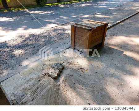 Wooden Box on Sandy Surface Near Roadway in Sunny Outdoor Environment With Trees 130343445