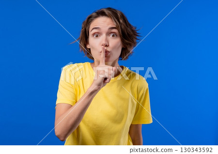 Beautiful woman makes shush shh gesture with finger on lips, silence signaling 130343592