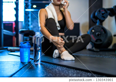 A woman taking a break and wiping sweat with a towel. A cool woman exercising at the gym. Hydration. Protein. 130343901