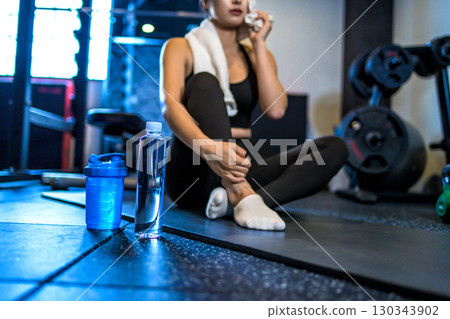 一位女士正在休息,用毛巾擦汗。一位酷酷的女士正在健身房鍛鍊。補充水分。補充蛋白質。 一位女士正在休息,用毛巾擦汗。一位酷酷的女士正在健身房鍛鍊。補充水分。補充蛋白質。 130343902