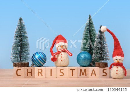 Christmas background with knitted snowmen in red hats and Christmas trees with turquoise ball and wooden cubes with the word Christmas on them. Christmas card. Christmas background with knitted snowmen in red hats and Christmas trees with turquoise ball and wooden cubes with the word Christmas on them. Christmas card. 130344135