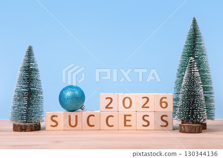 New Year 2026 and Christmas postcard. Wooden cubes with numbers 2026 and word success and green Christmas trees on a wooden table and a blue background. New Year 2026 and Christmas postcard. Wooden cubes with numbers 2026 and word success and green Christmas trees on a wooden table and a blue background. 130344136