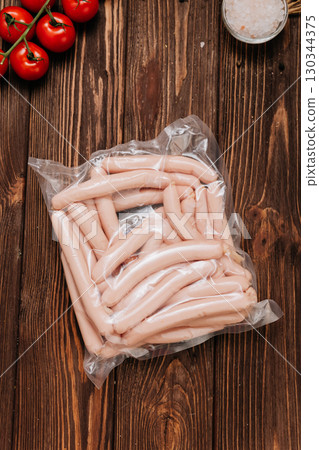 Vacuum packed chicken sausages on wooden table with tomatoes and salt in background Vacuum packed chicken sausages on wooden table with tomatoes and salt in background 130344375
