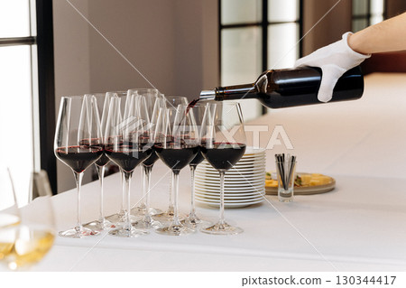 Red wine being elegantly poured into glasses during formal wine tasting event Red wine being elegantly poured into glasses during formal wine tasting event 130344417