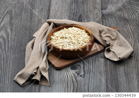 Oat flakes uncooked in a brown bowl on wooden table. Healthy food for breakfast Oat flakes uncooked in a brown bowl on wooden table. Healthy food for breakfast 130344439