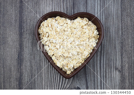 Oatmeal flakes and oats on a heart shaped plate on black background. Healthy breakfast. Organic and vegetarian food. 130344450