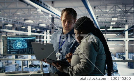 Team of data center programmers monitors deep learning process with laptop, reviewing operational metrics. Teamworking server hub colleagues review neural networks reports during inspection, camera B 130345200