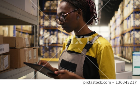 African american worker processing merchandise for business logistics system, busy warehouse space with industrial racks. Shipping protocols in online retail fulfillment center. Camera A. 130345217