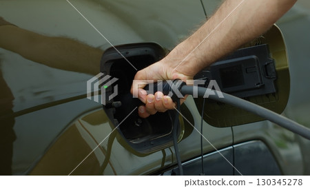Close up of driver recharging EV automobile battery powering green technology electric motor. Man recharges battery of EV car by plugging into alternative energy power source 130345278