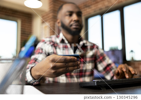 Closeup of male hands holding credit card and making secure online payment on computer. Black man shops digitally using banking website, typing information on desktop pc for convenient checkout. Closeup of male hands holding credit card and making secure online payment on computer. Black man shops digitally using banking website, typing information on desktop pc for convenient checkout. 130345296