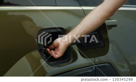 Close up of driver connecting EV plug to electric car to recharge it, concept of zero emissions technology. Man charging electric vehicle at EVSE station, showcasing green energy transportation Close up of driver connecting EV plug to electric car to recharge it, concept of zero emissions technology. Man charging electric vehicle at EVSE station, showcasing green energy transportation 130345299