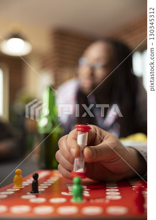 Close up on hand of caucasian man placing hourglass on board, ready to play. The image conveys relaxed, fun atmosphere, highlighting use of timer in playful context of friendly game. Close up on hand of caucasian man placing hourglass on board, ready to play. The image conveys relaxed, fun atmosphere, highlighting use of timer in playful context of friendly game. 130345312
