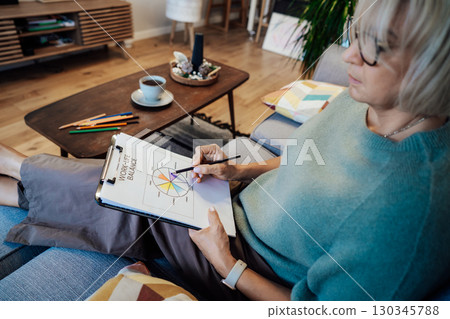 Woman drawing work-life balance wheel sitting on the sofa at home. Self-reflection and life planning for next new year. Personal Year review. Coaching tools. Finding Balance in Life. Selective focus. Woman drawing work-life balance wheel sitting on the sofa at home. Self-reflection and life planning for next new year. Personal Year review. Coaching tools. Finding Balance in Life. Selective focus. 130345788